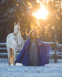 Winter Wonderland Shooting im Schnee mit Schimmel Pferd und Frau in Mantel und Kleid. Aschenputtel Thema